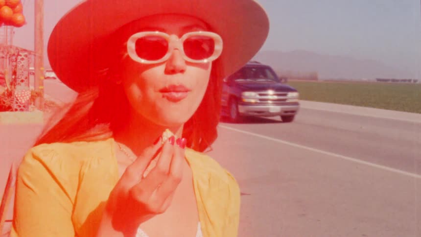 Young woman wearing a hat and sunglasses eating on a roadside shop