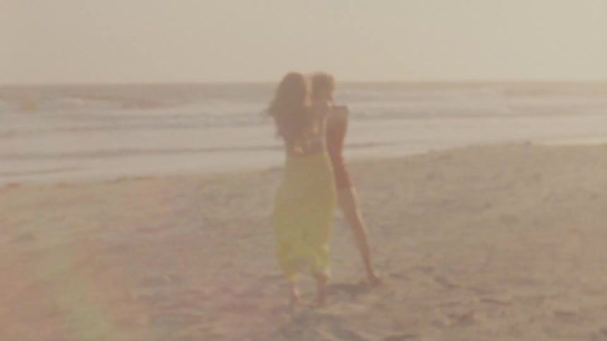 Two women hold hands and twirl leaning back on the beach in the bright sunshine