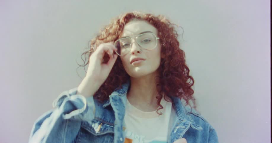 A model posed against a wall lowers her eyeglasses and winks at the camera