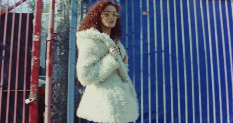 A woman holds her jacket and poses as she walks on a city sidewalk