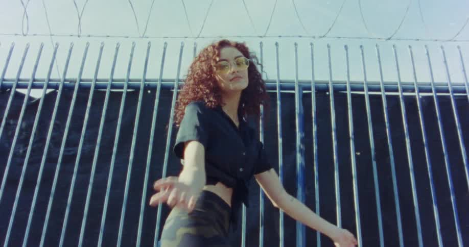 A woman dancing outside near a fence with barbed wire on top