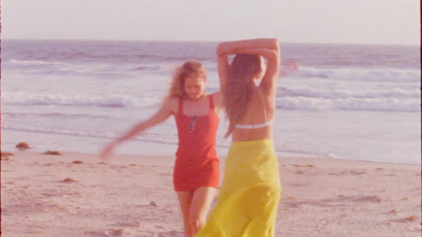 Two women move across beach posing