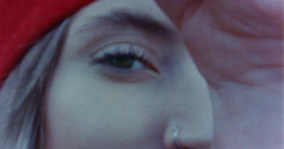Close up of the eye of a woman wearing a red hat seen through her hands