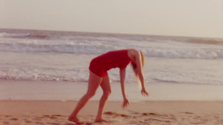 A woman smiles as she does a cartwheel on the beach sand