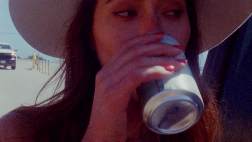 A woman wearing a hat is drinking a beverage from a can outside on a sunny day