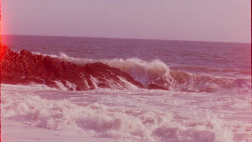 Ocean waves are crashing onto rocks on a beach on a sunny day