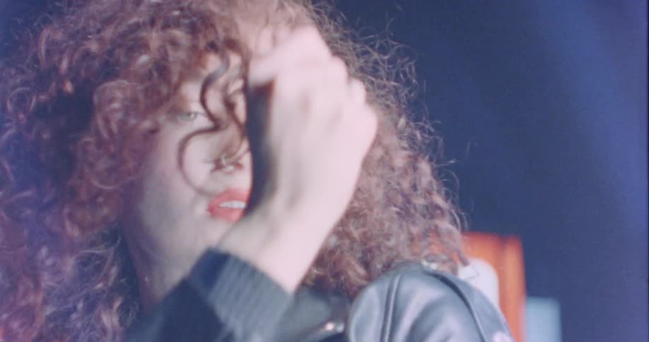 A young woman with curly red hair is dancing and posing