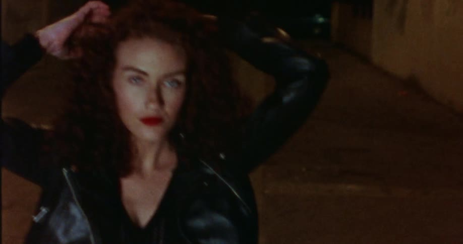A woman throws her arms up as she dances in an alley