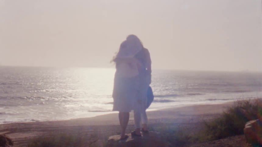 Two women hug on the windy beach