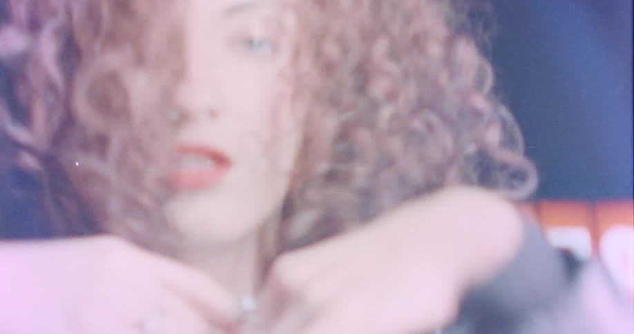 Woman with red curly hair and black leather jacket dances in front off billboard at night