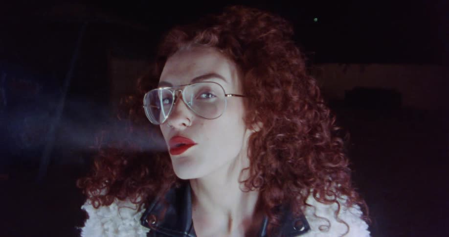A woman stands outside at night and smokes