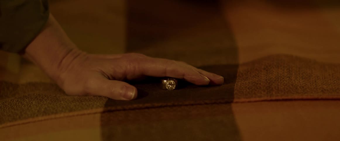 Woman with brown shirt touches ring on bed in bedroom