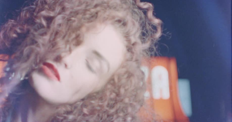 Young girl with curly hair modeling in front of a sign on the street at night