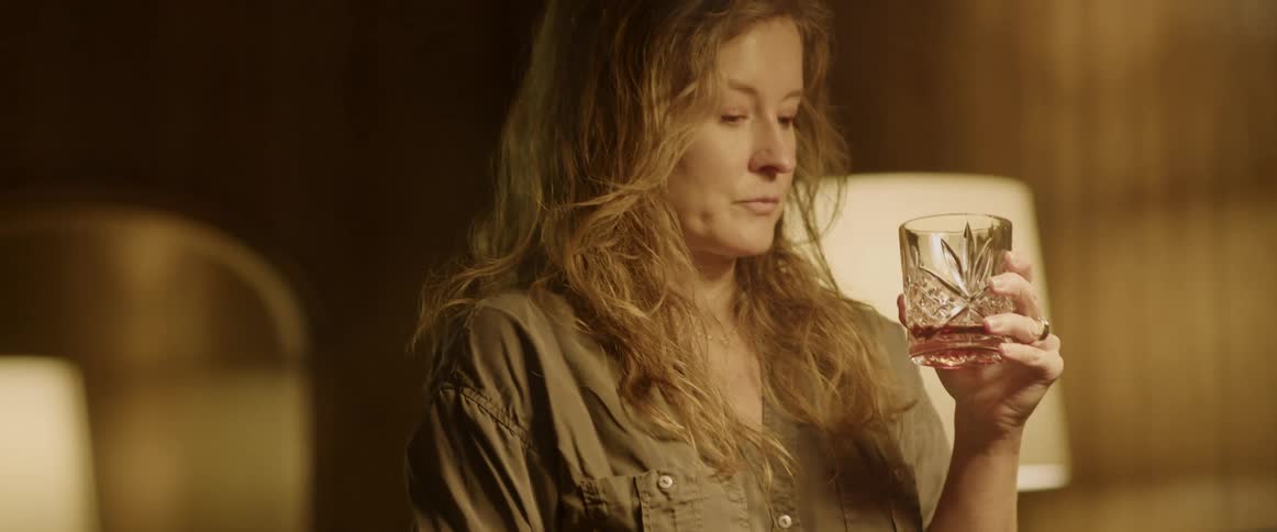 A woman is lifting a glass with alcohol to her lips to take a drink