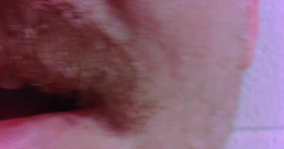 Close up of the mouth of a man with a mustache standing against a white brick wall
