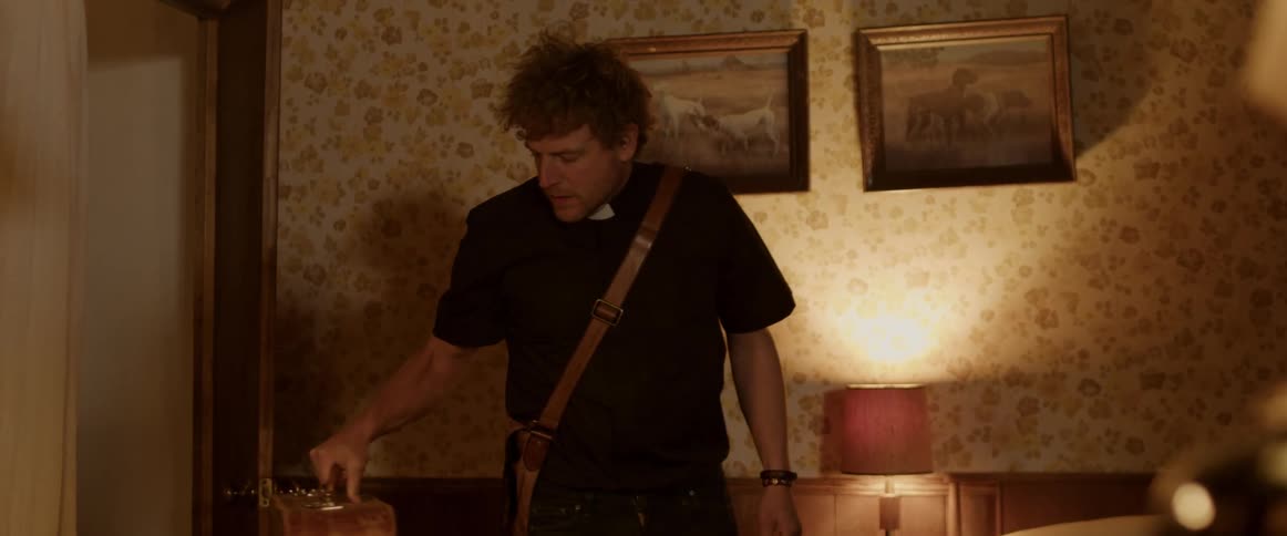 A priest enters the room with his bag