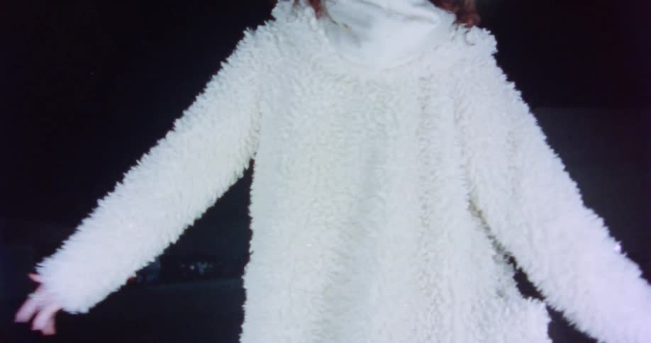 A woman wearing a white hooded jacket walks on a line in parking lot with her arms extended