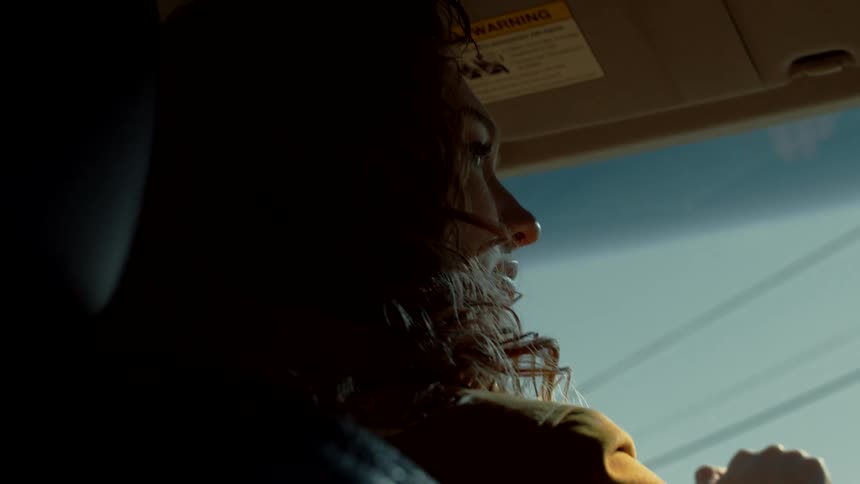 Young woman with curly hair driving a car under a blue sky