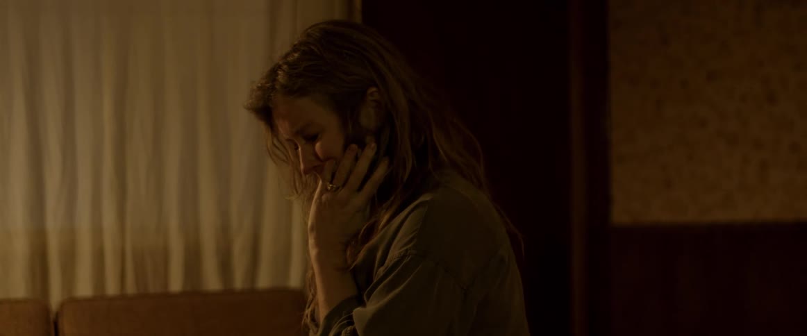 A woman with long brown hair is alone in a room crying