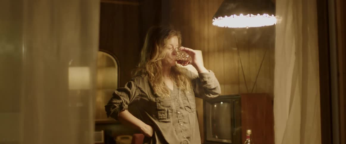 Woman stand near table holding a liquor bottle taking a drink