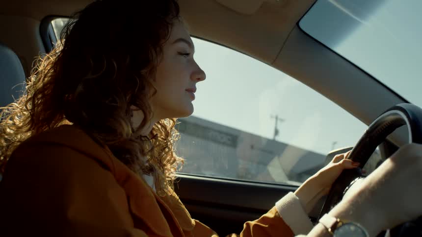 A woman smiles as she drives her car forward
