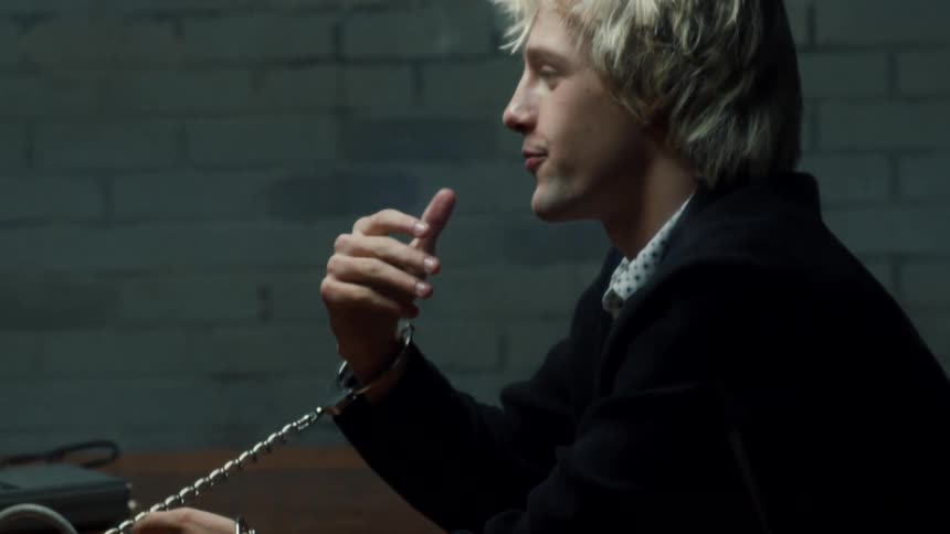 A man is handcuffed to a desk and is talking