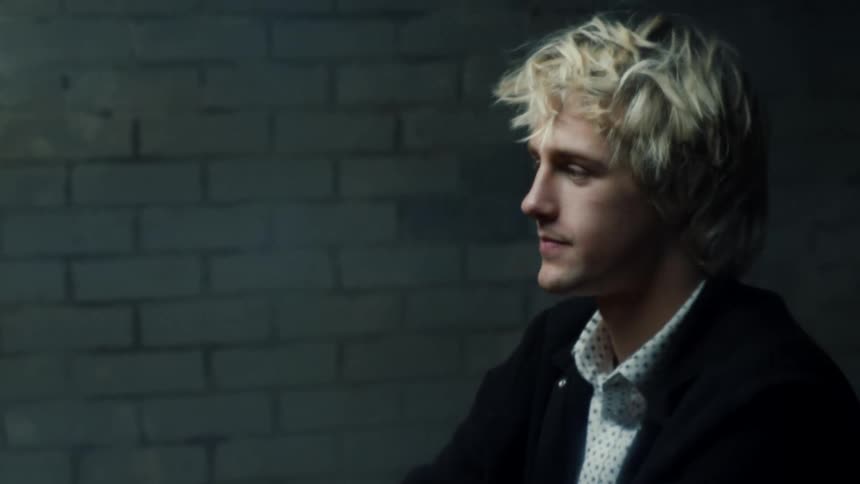 A man is sitting in a room near a brick wall