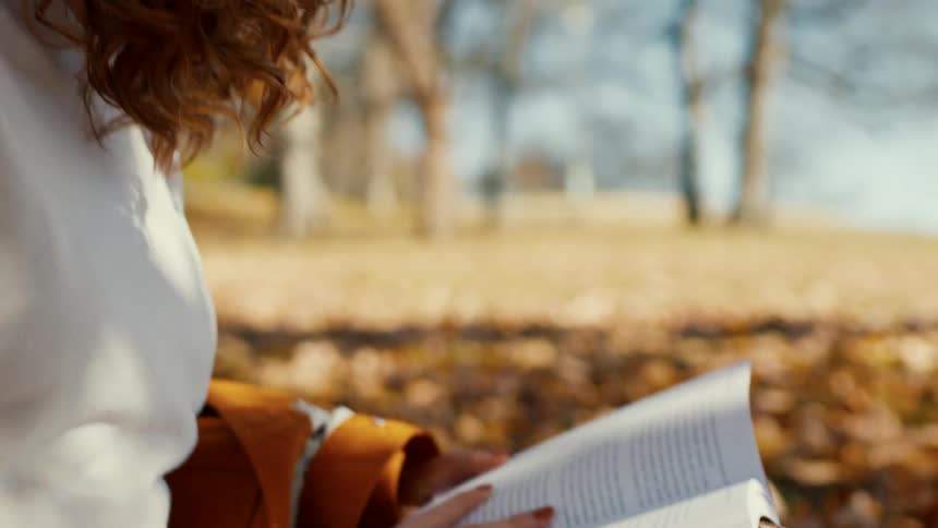 A woman is sitting on the field in the park reading a book