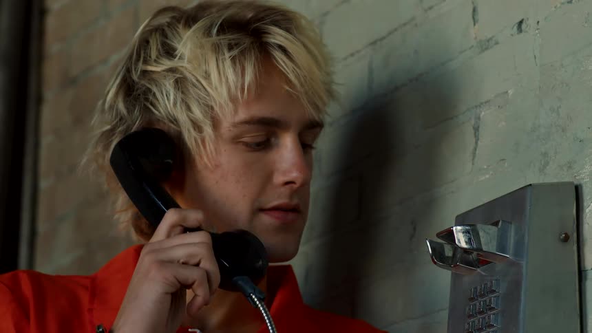 A man in handcuffs holds a phone against his face and then sadly hangs up