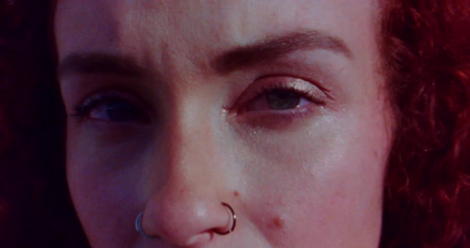 Eye closeup of a redhead young woman with a piercing on her nose reclined on a white brick wall