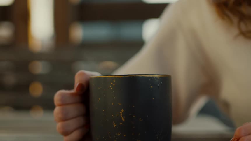 A woman is holding a black mug of steaming hot coffee