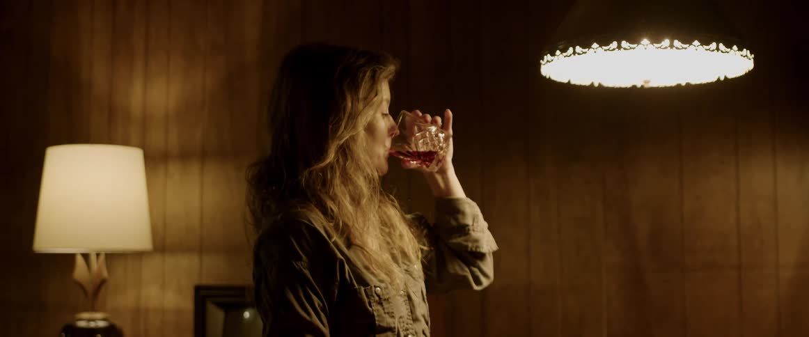 A woman is standing in a room and taking a drink of alcohol from a glass