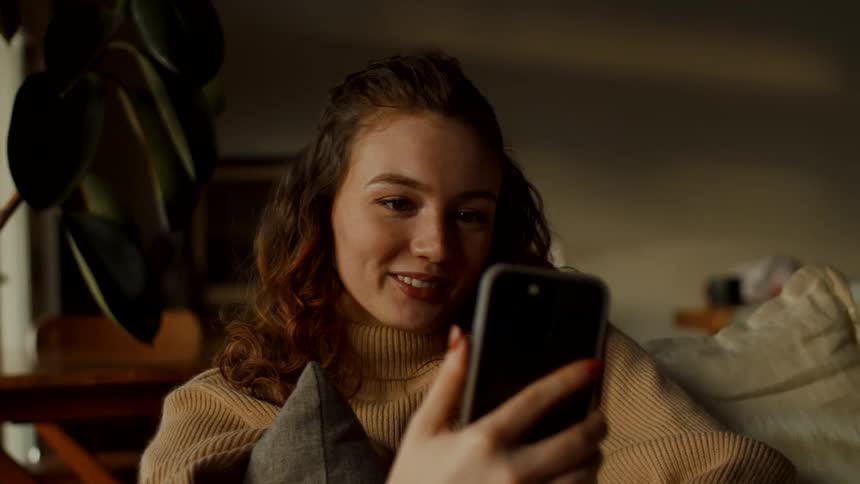 Woman sits on couch smiling as she video call on her mobile phone