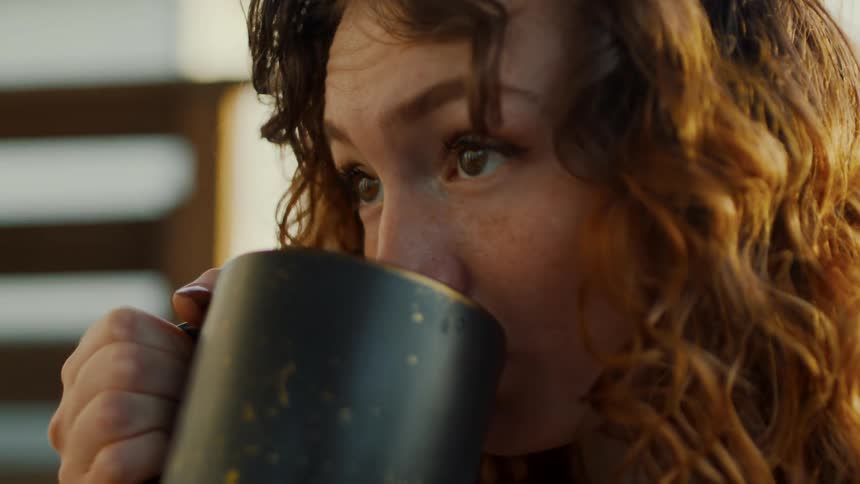 A woman is sitting indoors and drinking coffee