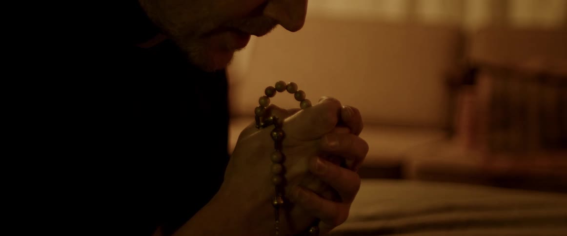 Man leans over praying with a rosary