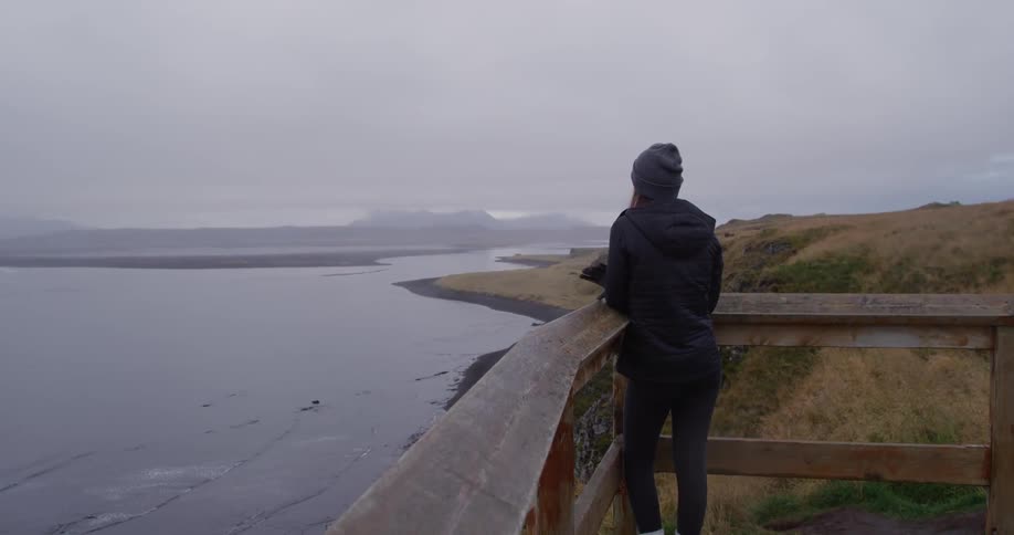 A woman leans on a balcony overlooking a coast line