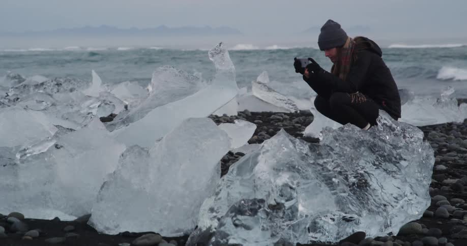 A person photographing large pieces of ice up close on the shore