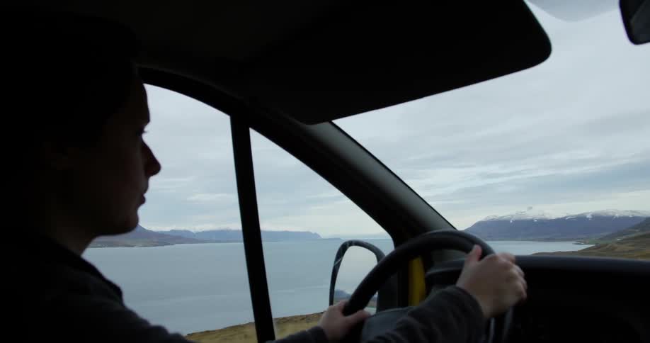 A woman is driving a car near the water
