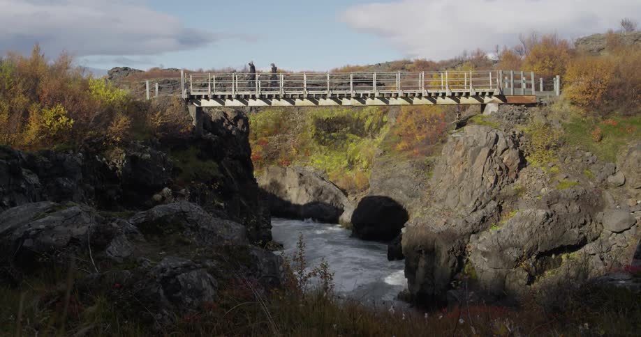 Two people walk across a small bridge over a stream