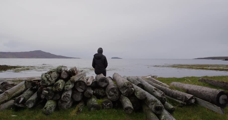 Man looks toward the water while standing near a log pile