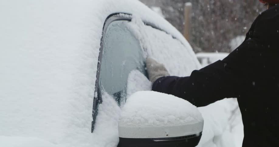 A woman wipes the snow from her car window