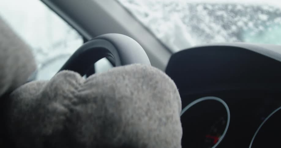 Hands wearing mittens turning steering wheel in the snow