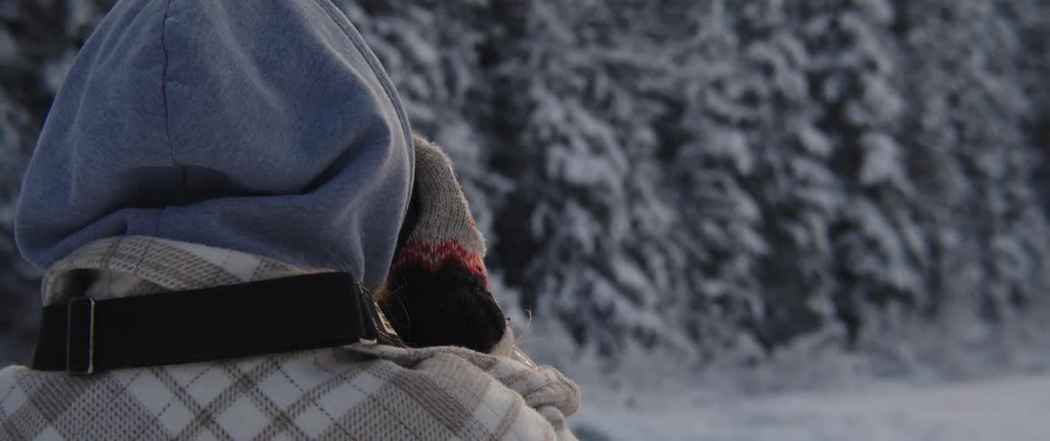 A person looking out at a snow covered trail and trees with hands holding a camera or binoculars