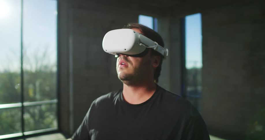 A man is wearing a headset and moving his head and arm around while playing a virtual reality game