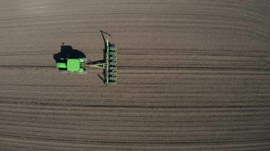 Aerial view of green tractor tilling field