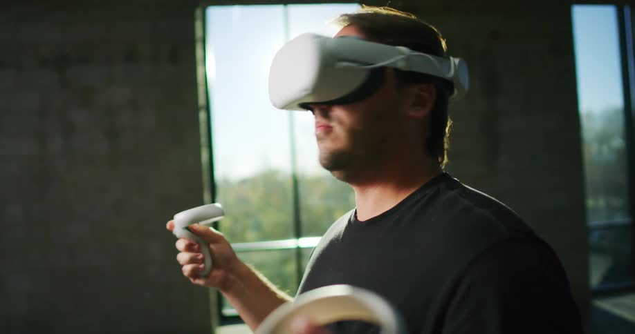 A man wearing a virtual reality headset has a controller in each hand as he plays a game