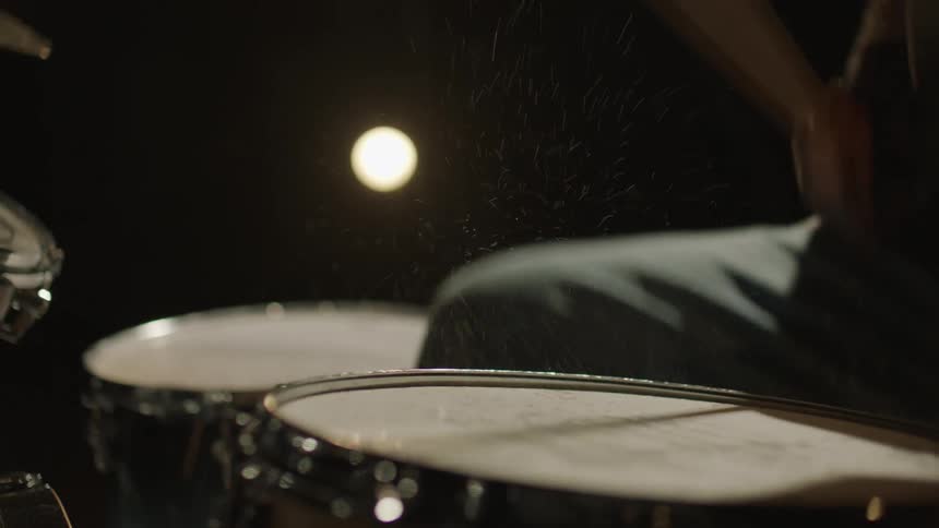 Water bounces off wet drums as man plays the drums at night