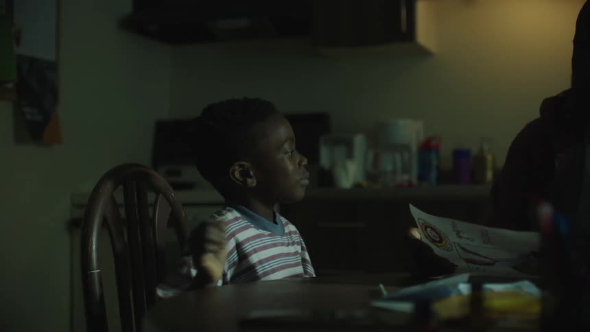 A boy walks over to the table to show his father a piece of paper