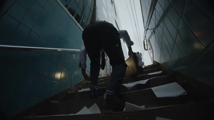 A man tries to pick up papers and stuff them back inside his briefcase as he gets snowed on in a stairwell