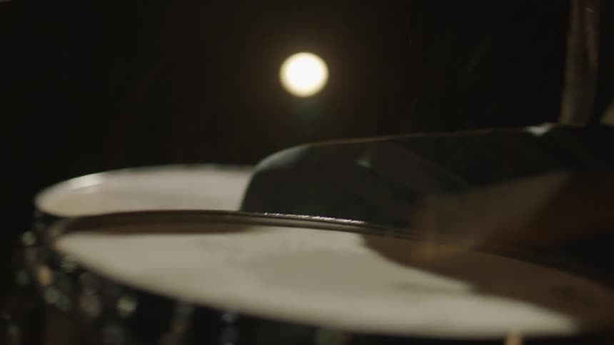 A man drums in a dark room with spotlights
